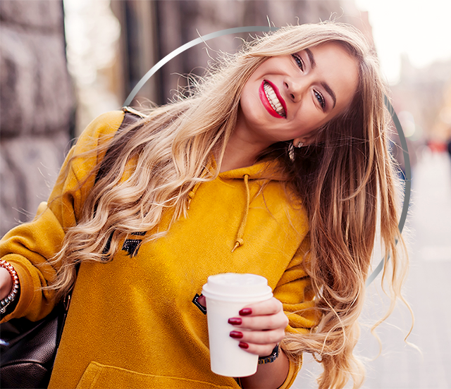 Sretna mlada žena u žutoj majici s kapuljačom drži papirnatu čašu za kavu.