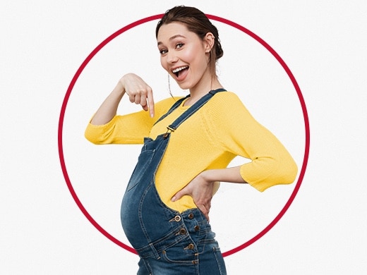 Nasmiješena mlada trudnica u žutoj vesti pokazuje na svoj trbuščić